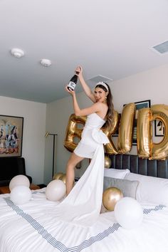 a woman standing on top of a bed in front of giant gold letters and balloons