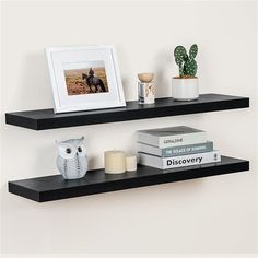 two black floating shelves with books, candles and an owl figurine on each shelf