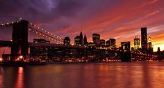 the city skyline is lit up at night as seen from across the water in front of an orange and purple sky