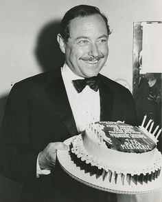 a man in a tuxedo holding a birthday cake