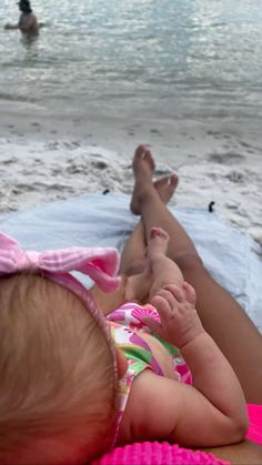 a baby laying on top of a beach next to the ocean