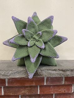 a green and purple knitted star decoration sitting on top of a brick wall