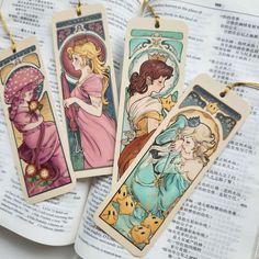 three bookmarks with pictures of women and cats on them, sitting next to an open book