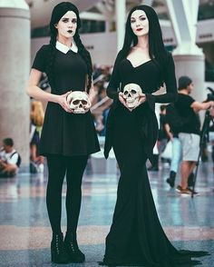 two women dressed in black holding skulls and posing for the camera with their hands on their hipss