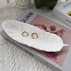 two wedding rings sitting on top of a white feather shaped tray next to a book