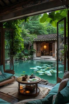 a living room filled with lots of furniture next to a swimming pool surrounded by greenery