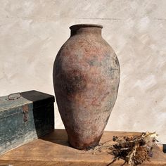 an old vase sitting on top of a wooden table next to a trunk and box