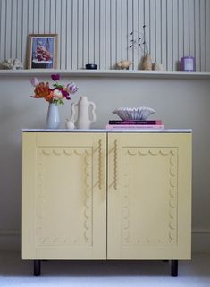 a yellow cabinet with some vases and flowers on top of it in front of a white wall