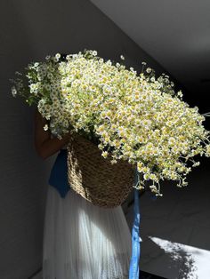 a woman holding a basket full of flowers on top of her head while standing next to a wall