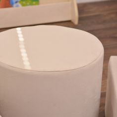 a close up of a white round ottoman on a wooden floor with other furniture in the background