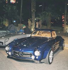 two cars parked next to each other on a street at night with palm trees in the background