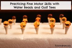 several yellow glass beads are lined up on a white surface with the words practicing fine motor skills with water beads and golf tees