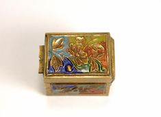 an ornate gold and enamel box with flowers on the front, sitting on a white surface