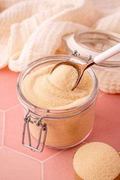 a jar filled with powder next to two spoons on a pink tablecloth covered floor