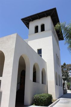 a white building with an arched doorway and clock on the top floor is next to a palm tree