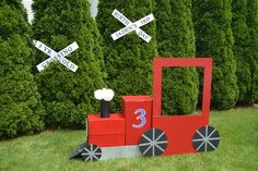 a train made out of cardboard is sitting in the grass next to some bushes and street signs