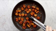 someone is frying tofu in a skillet with tongs