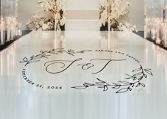 a wedding ceremony aisle with candles and flowers on the floor in front of an ornate monogrammed sign