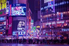 many people are standing in the middle of a busy city street at night with neon lights