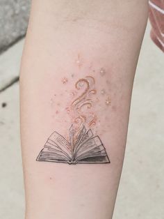 an open book tattoo on the arm with stars coming out of it's pages