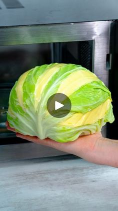 a hand holding up a head of cabbage in front of an open microwave oven door