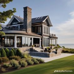 a large house sitting on top of a lush green field next to the ocean with lots of windows