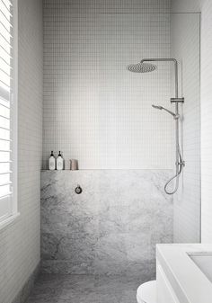 a white tiled bathroom with a shower, toilet and bathtub in the corner next to it