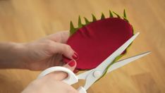 a person cutting fabric with scissors on top of a wooden table next to a red heart