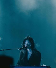 a woman with long hair standing in front of a keyboard on stage holding a microphone