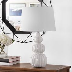 a white lamp sitting on top of a wooden table next to a mirror and vase