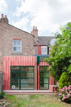 a red brick building with green glass doors and windows on the outside, surrounded by greenery