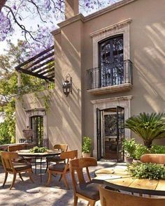 an outdoor dining area with tables and chairs under a purple flowering tree in front of a house