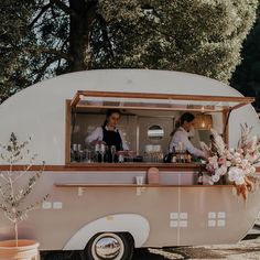 two people standing at the counter of a food truck with flowers on it's side