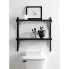 a black shelf above a toilet in a bathroom with a plant on the tank lid