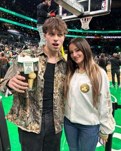 a man and woman standing next to each other in front of a basketball hoop holding beers