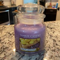 a purple candle sitting on top of a counter next to a glass jar filled with lemons