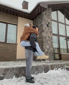 a man carrying a child in front of a house with snow on the ground and steps