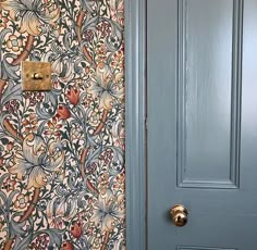 a blue door with an ornate wallpaper in the background and a gold handle on it