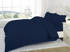 a bed with blue sheets and pillows in a room next to a white nightstand table