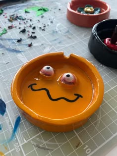 an orange bowl with two faces painted on it and other bowls in the back ground