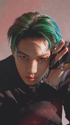 a young man with green hair is holding his hand up to his ear and looking at the camera