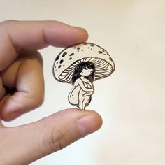 a person holding up a brooch with a mushroom on it