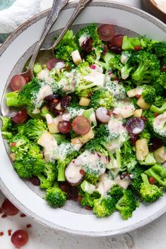 a bowl filled with broccoli, grapes and dressing on top of a table