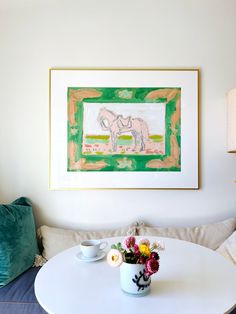 a white table with flowers and two cups on it in front of a framed painting