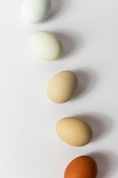 four eggs lined up in a row on a white surface with one orange and the other brown