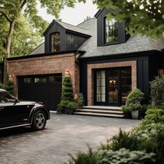 a black car is parked in front of a house with trees and bushes around it