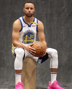 a basketball player sitting on top of a box with a ball in his hand and wearing pink shoes