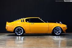 an orange car parked in a garage next to a black wall and some white rims