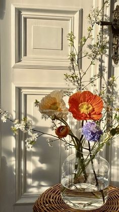 an arrangement of flowers in a glass vase on a wicker table next to a door