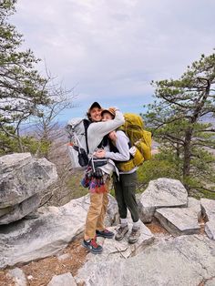 two people standing on top of a mountain with backpacks over their shoulders and arms around each other